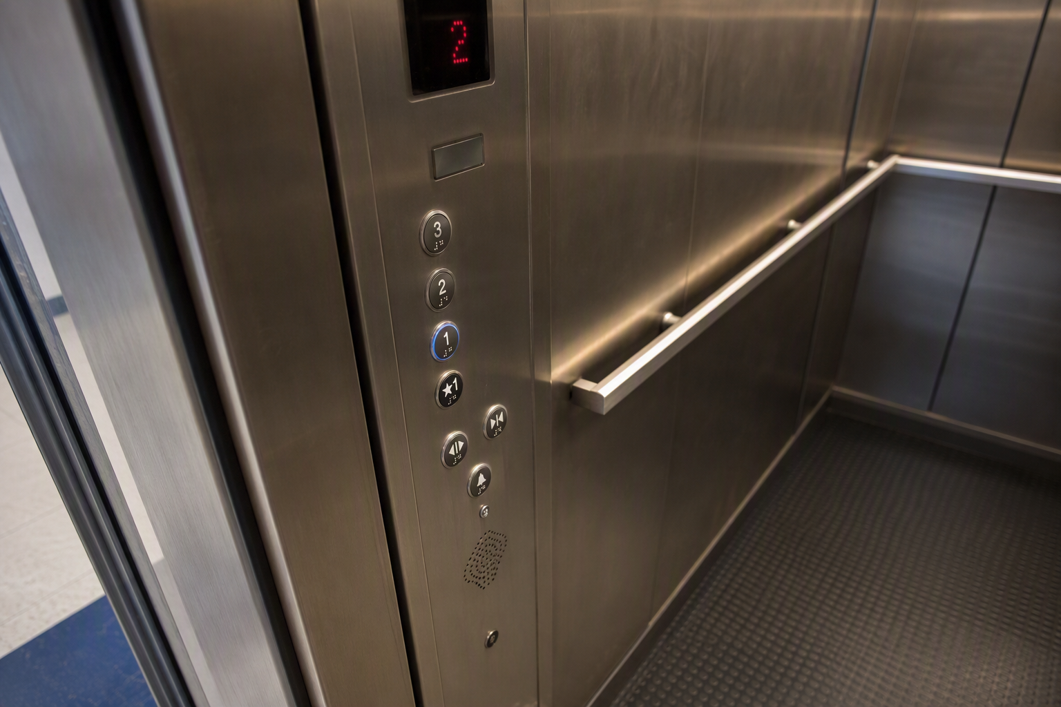 Interior ADA-compliant elevator control panel in a Florida K-12 school showing tactile Braille buttons, emergency communication system, and floor indicator display