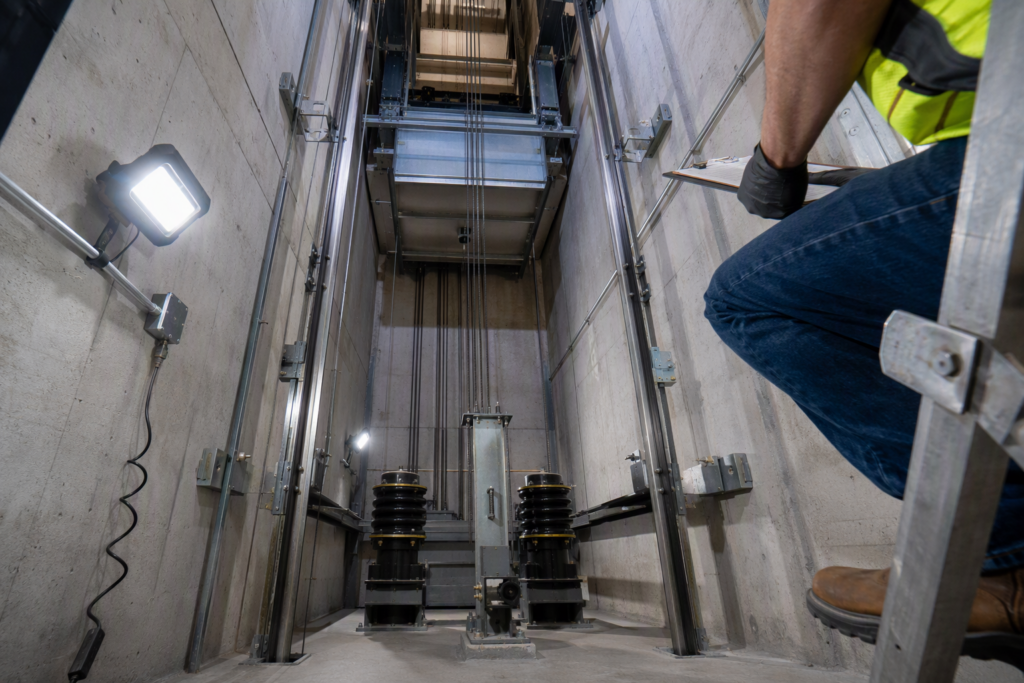 Licensed Florida elevator inspector examining pit safety components during a code-required elevator inspection in a Pompano Beach commercial building, checking buffers and stop switches