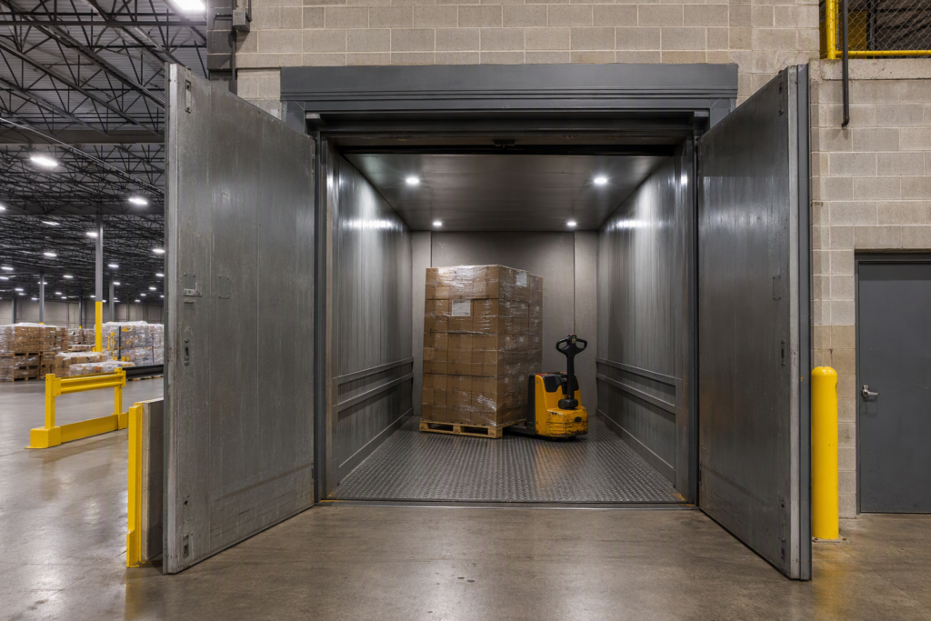 Heavy-duty industrial freight elevator with bi-parting steel doors open and loaded pallet inside a Florida warehouse facility rated for heavy freight capacity