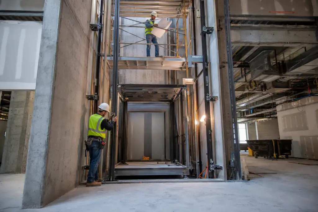 Commercial elevator installation in a Florida mid-rise office building hoistway, showing guide rails, cab frame, and workers during the multi-month installation process